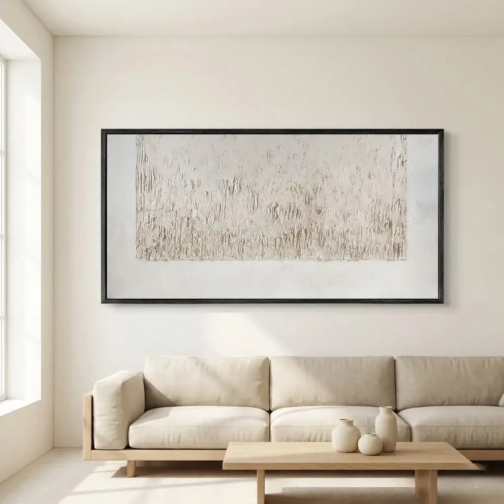 Beige abstract painting in a black frame on a white wall above a beige sofa in a living room.
