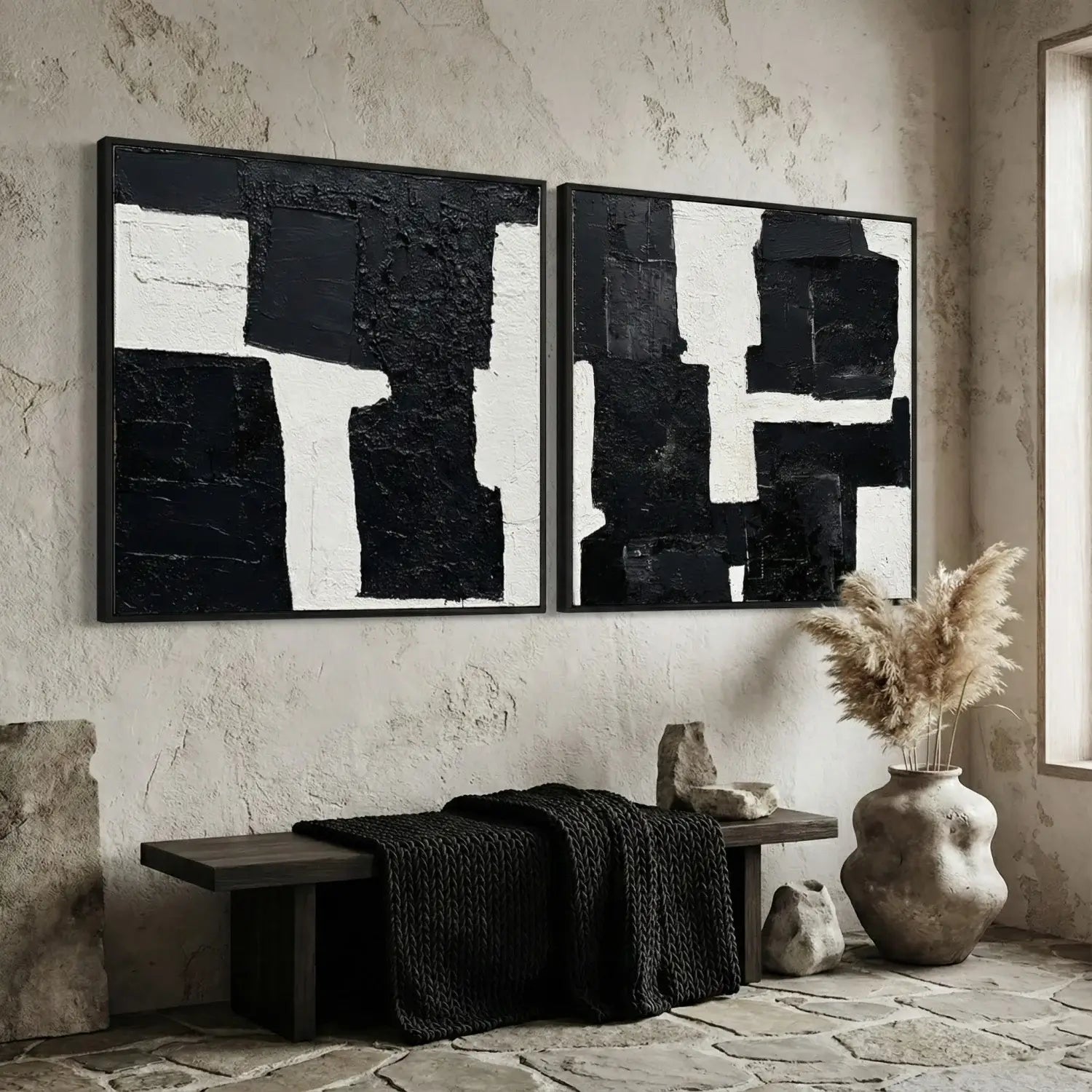 Abstract black and white paintings on a textured wall with a bench and decorative items below.