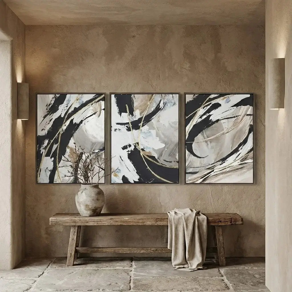 Three abstract paintings on a wall above a wooden bench with a vase and cloth.