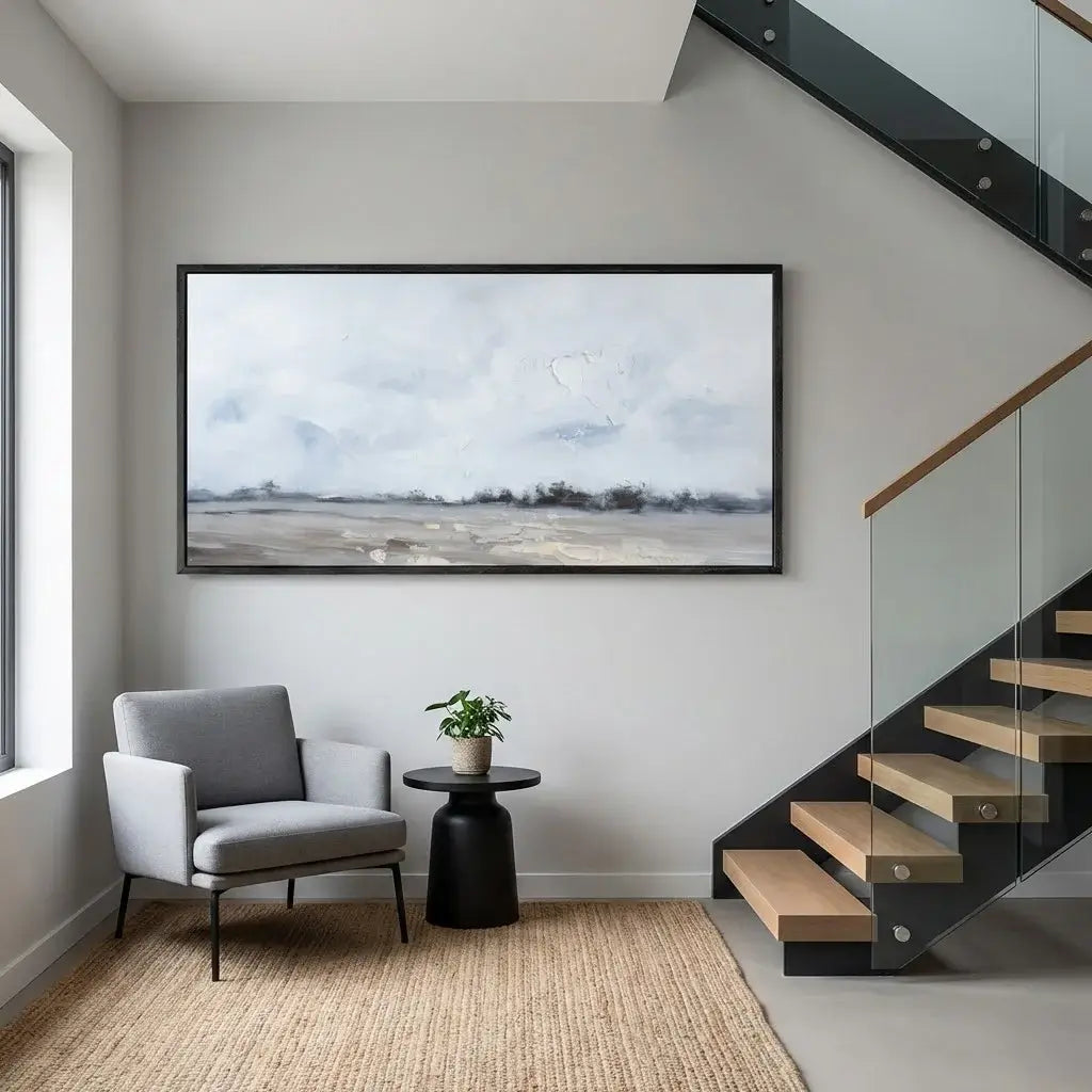 Modern interior with a gray armchair, round black table, and large framed picture on a white wall.