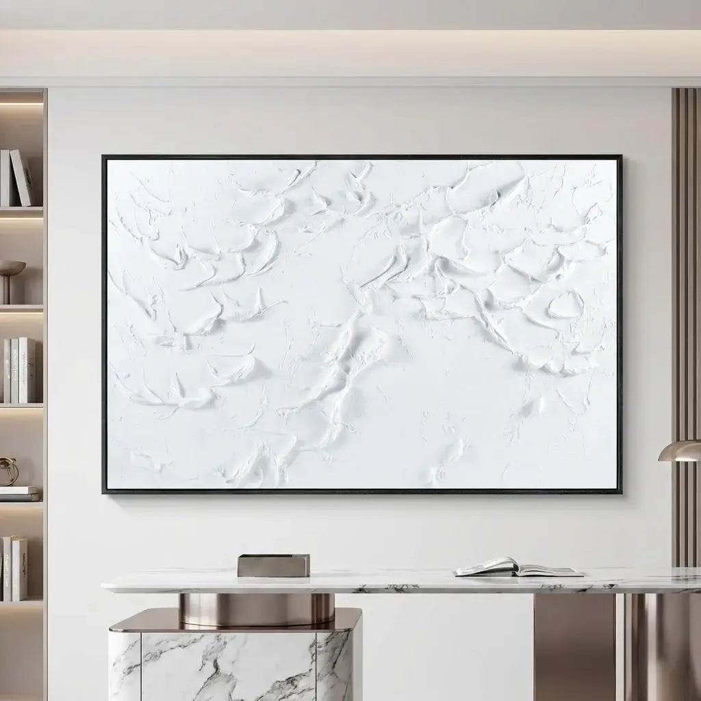 Abstract white painting on a wall in a modern interior setting with a bookshelf and table.