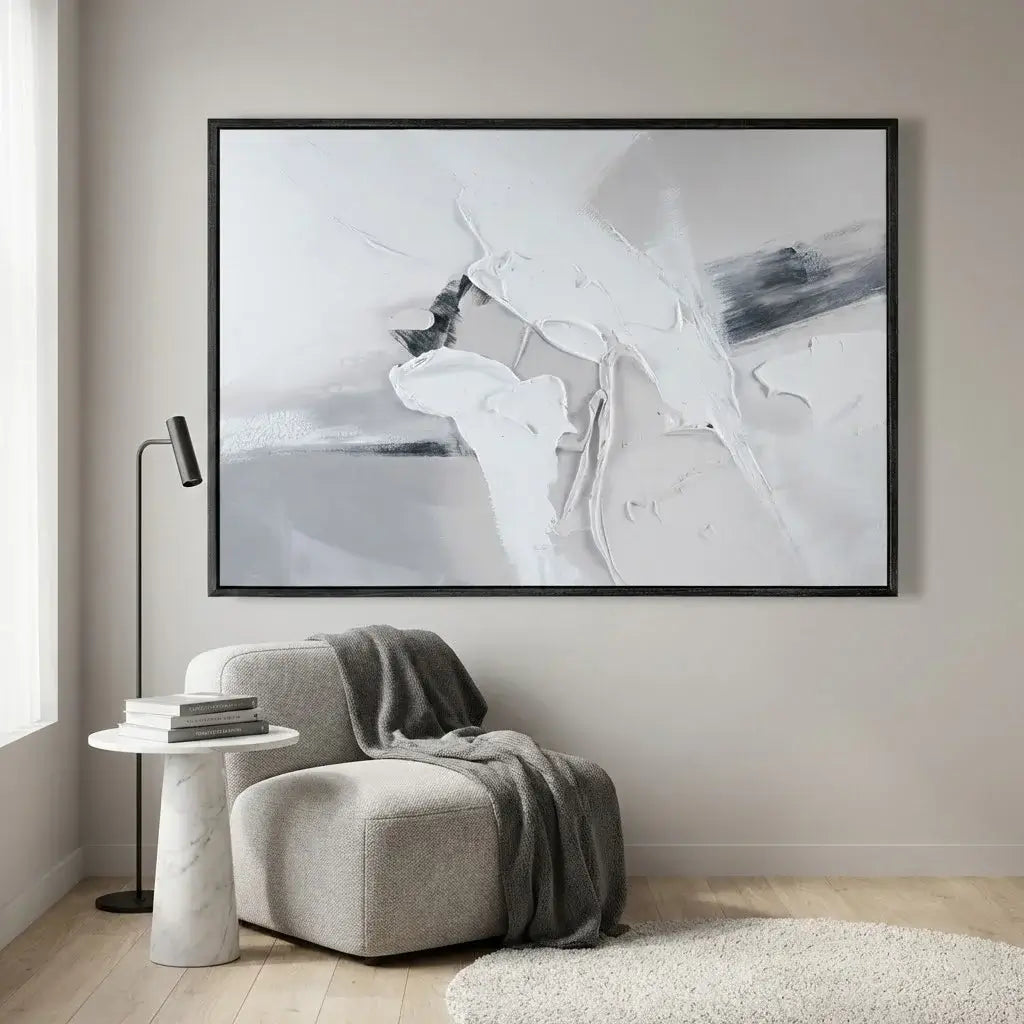 Abstract art piece in a black frame on a wall above a gray armchair.