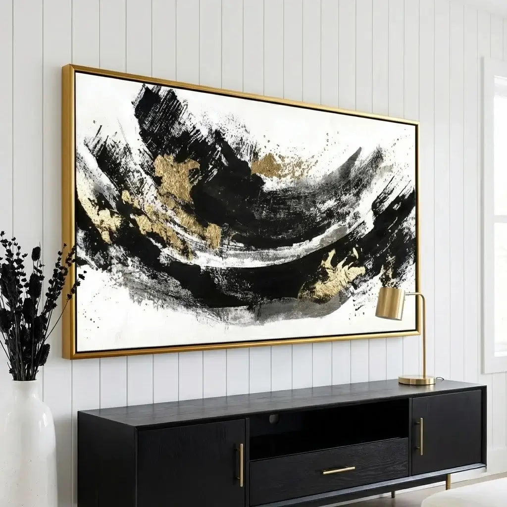 Abstract art piece with gold accents in a gold frame on a white wall above a black entertainment console.