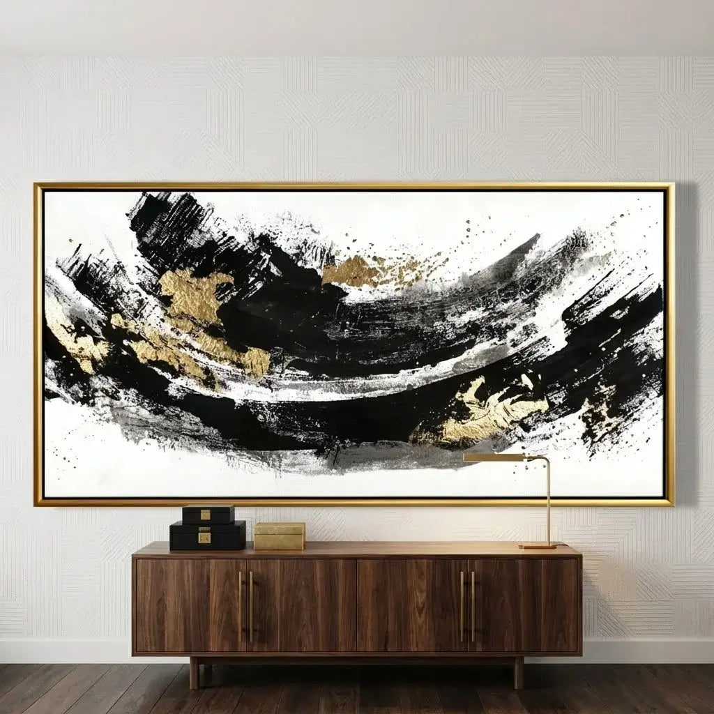 Abstract art piece with black and gold brush strokes in a gold frame on a wall above a wooden cabinet.