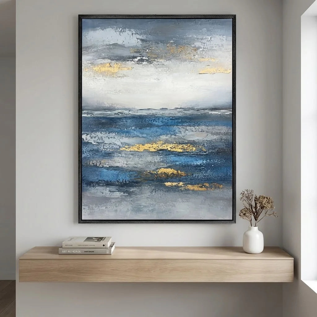 Abstract painting with blue and gold tones on a wall above a wooden shelf.
