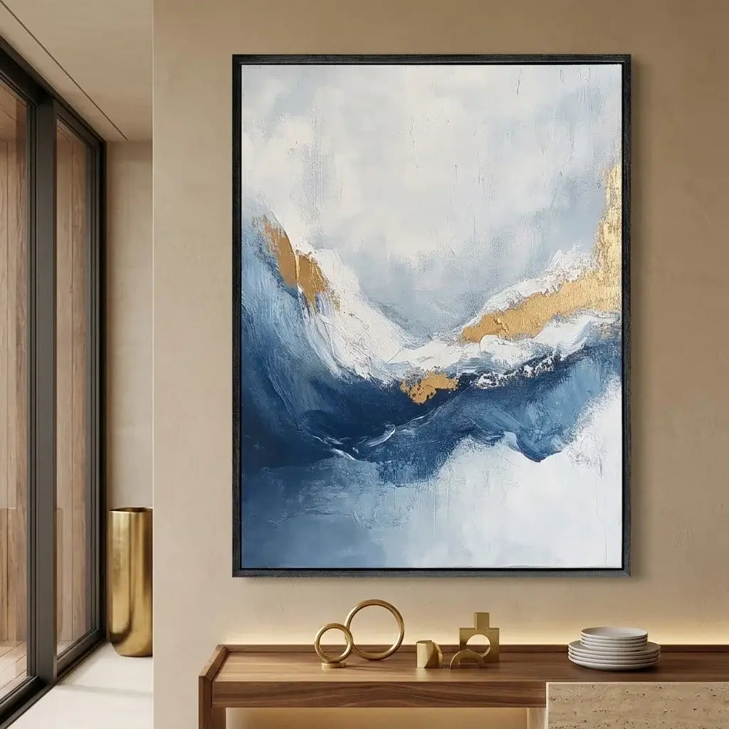 Abstract painting with blue and gold tones on a beige wall above a wooden table.