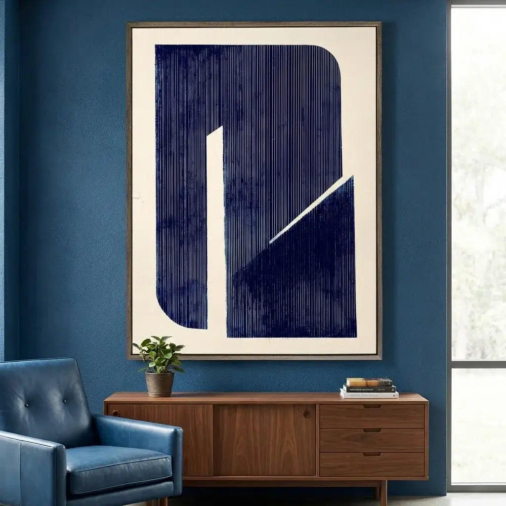Abstract art piece on a blue wall with a blue armchair and wooden cabinet below.