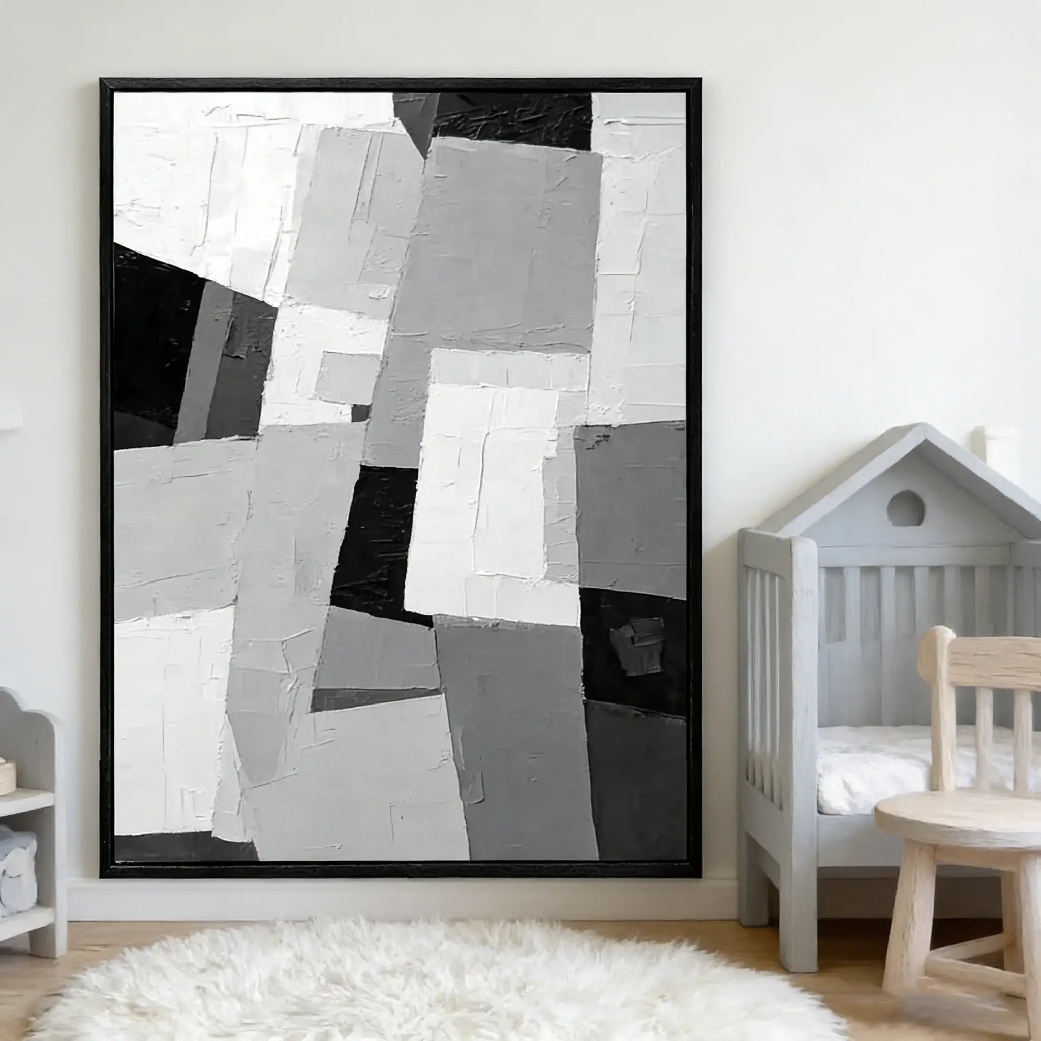 Abstract art piece in a black frame on a wall above a crib.