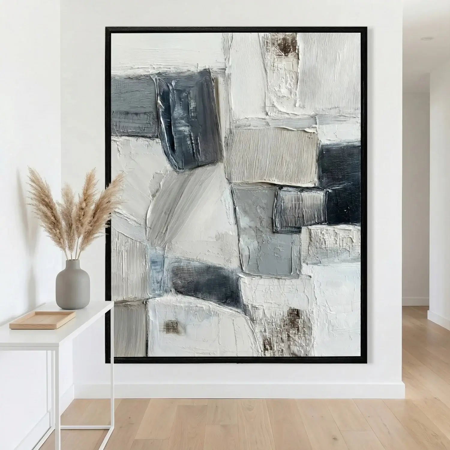 Abstract art piece in a black frame on a wall with a vase and decorative items below.