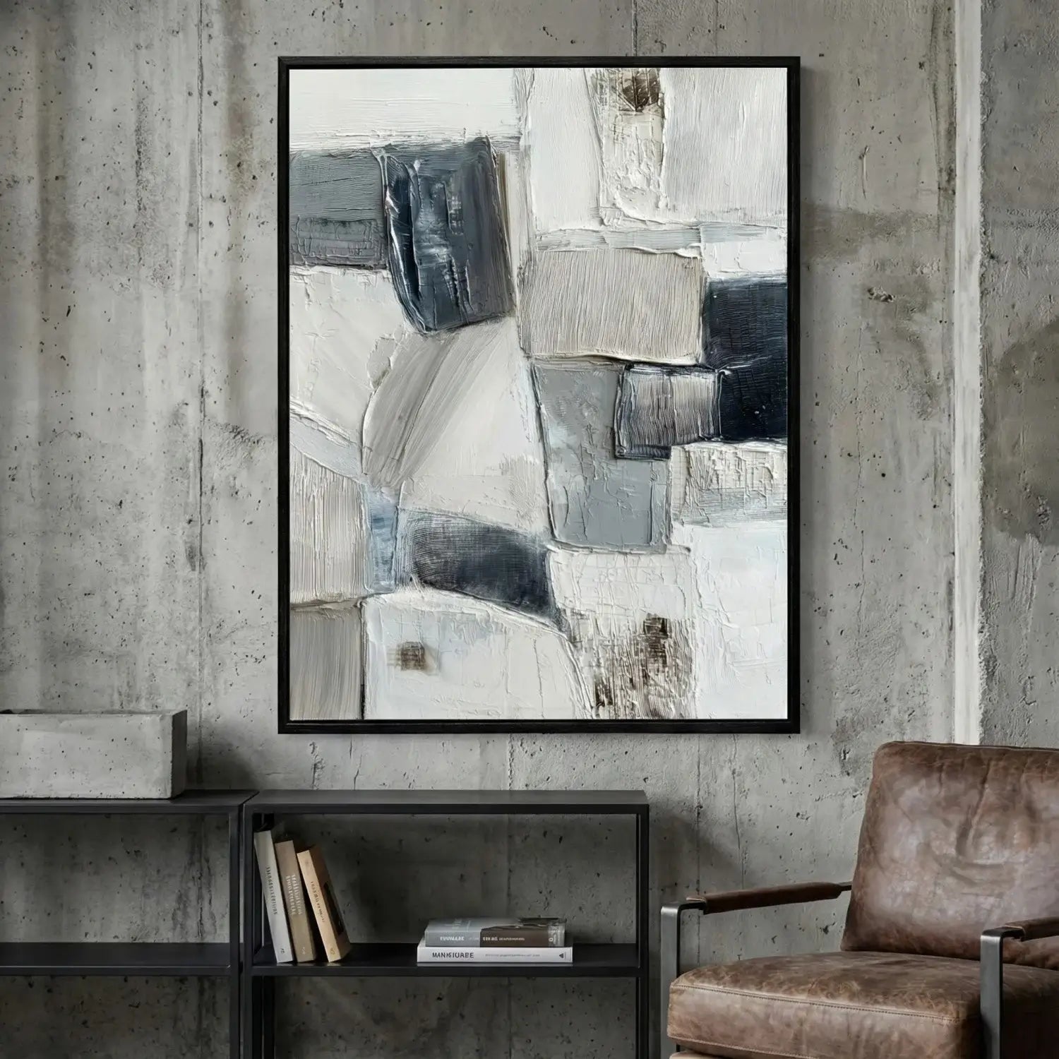 Abstract art piece in a black frame on a concrete wall with a chair and shelf below.