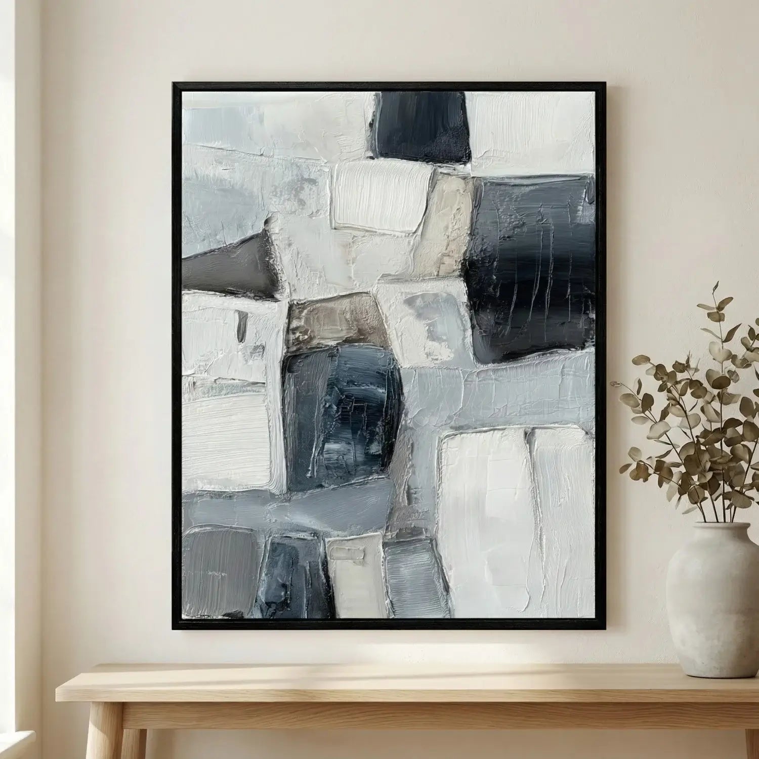 Abstract art print in a black frame on a wall above a wooden table with a plant.