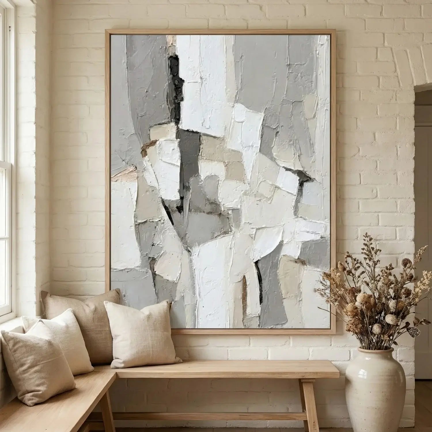 Abstract art piece on a wall above a wooden bench with pillows in a room with white brick walls.
