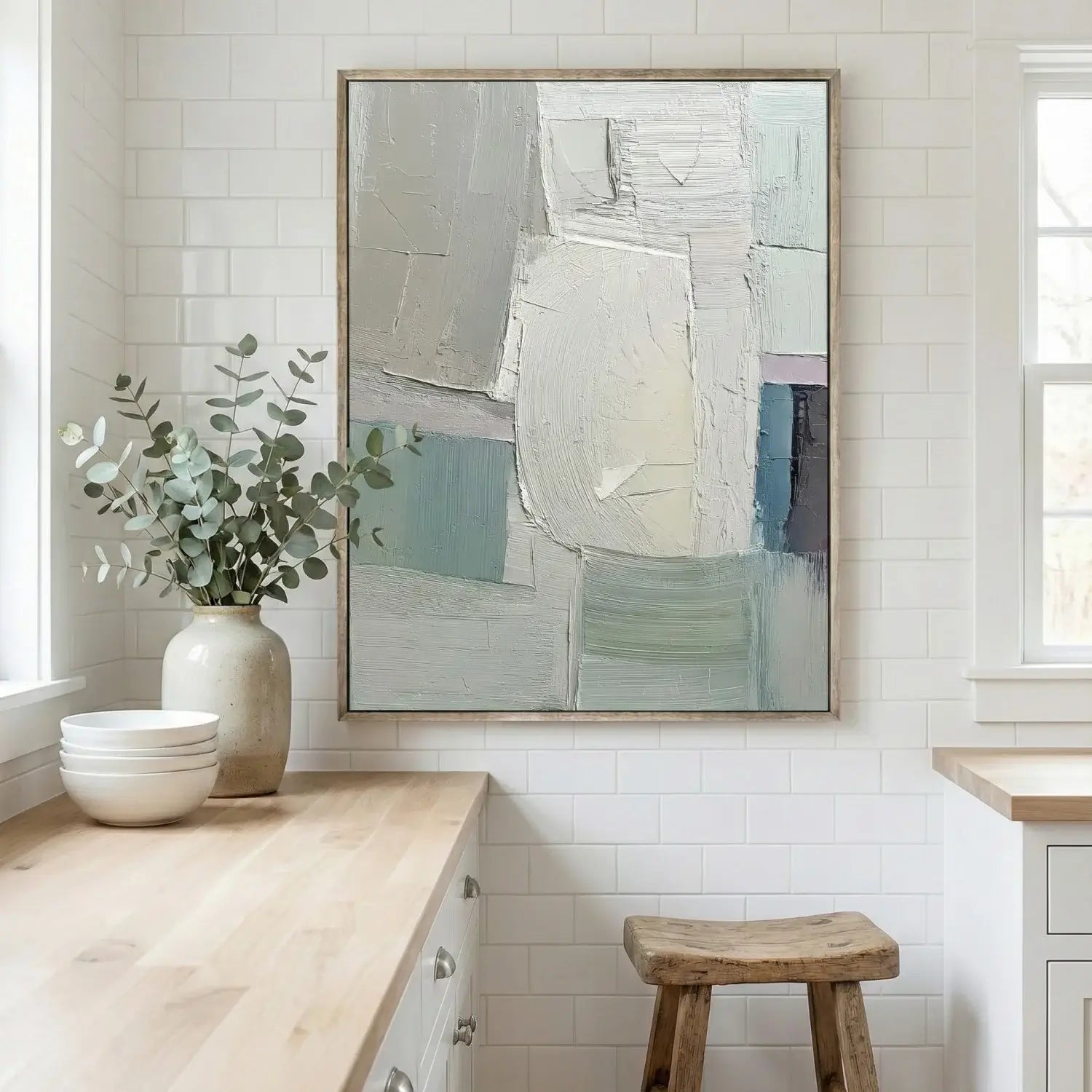 Abstract painting in a modern kitchen with a vase of greenery and wooden stool.