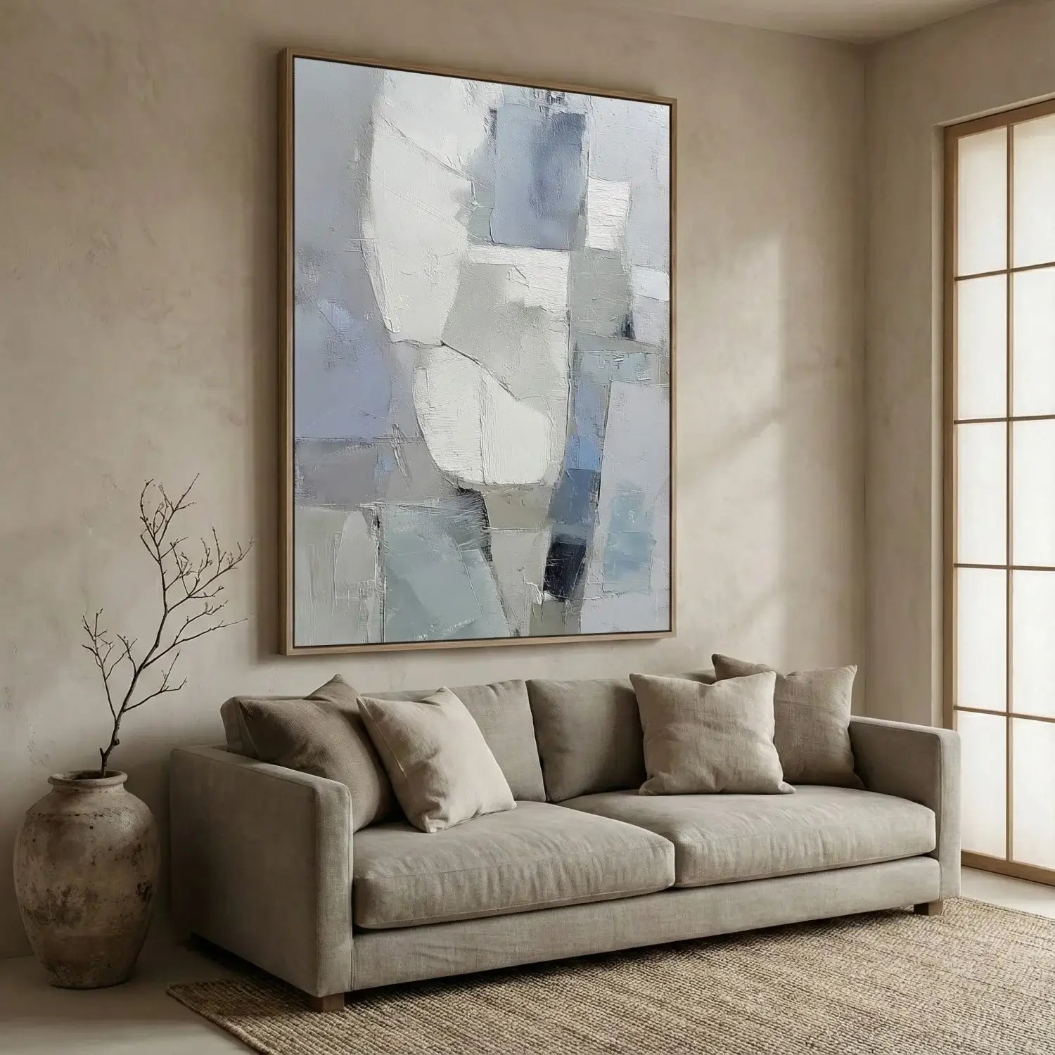 Gray sofa in a living room with abstract art above it and a vase on the floor.