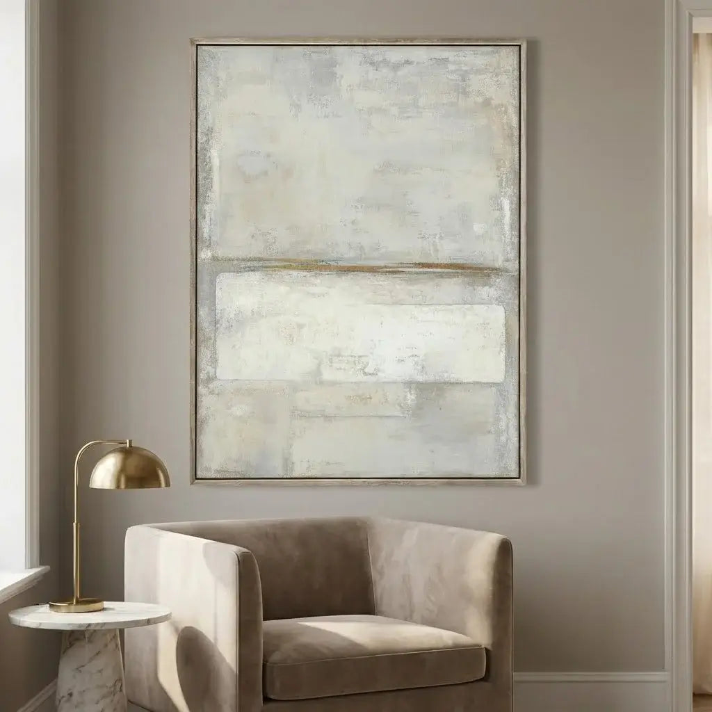 Abstract painting on a wall above a beige armchair with a gold lamp.
