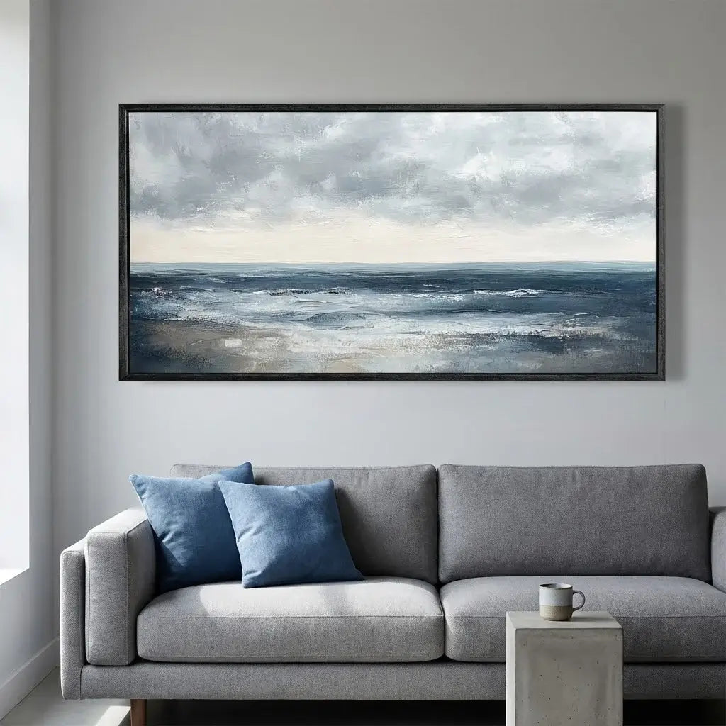 Framed artwork of a seascape above a gray sofa with blue pillows in a living room.