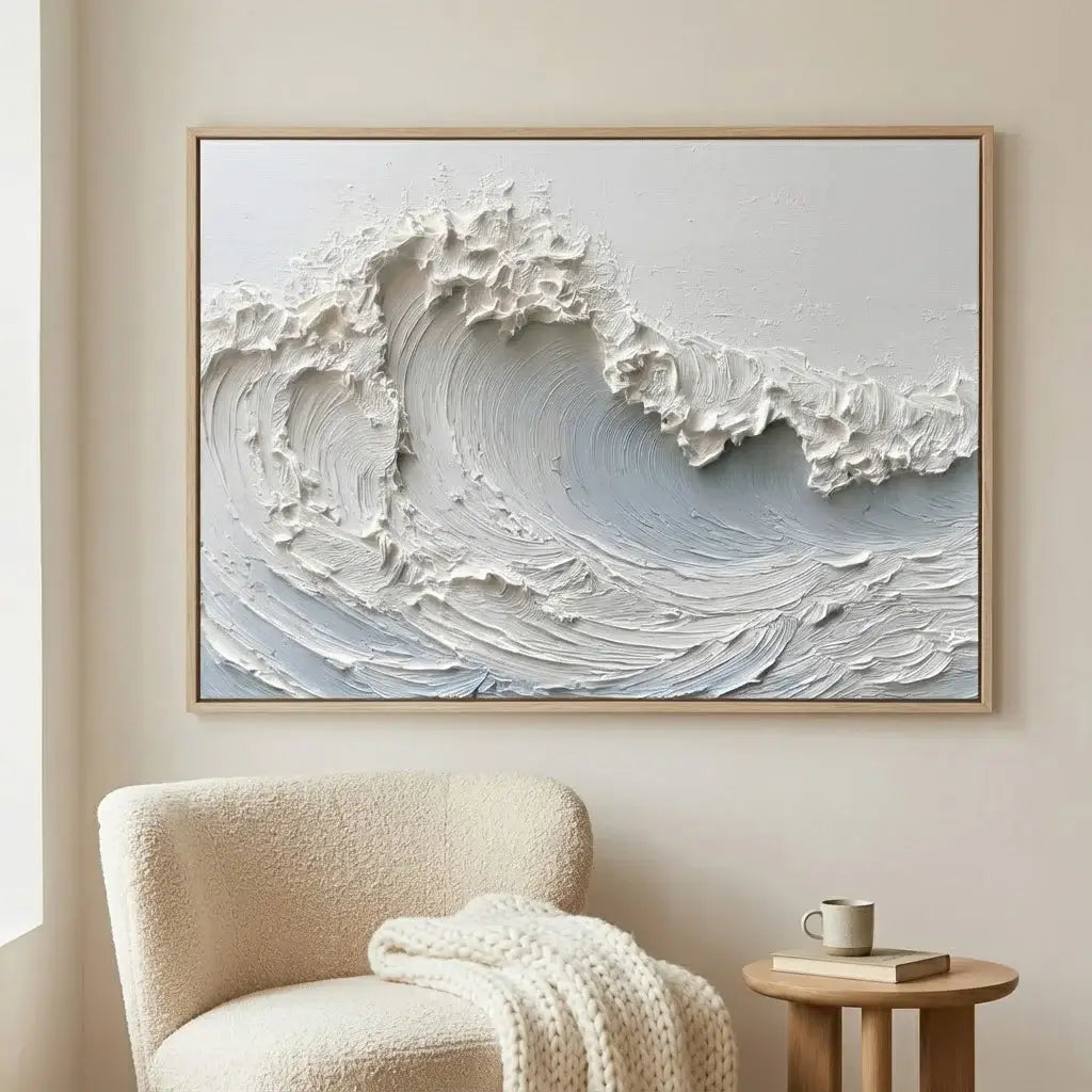 Framed artwork of a wave on a wall above a chair with a blanket and small table.