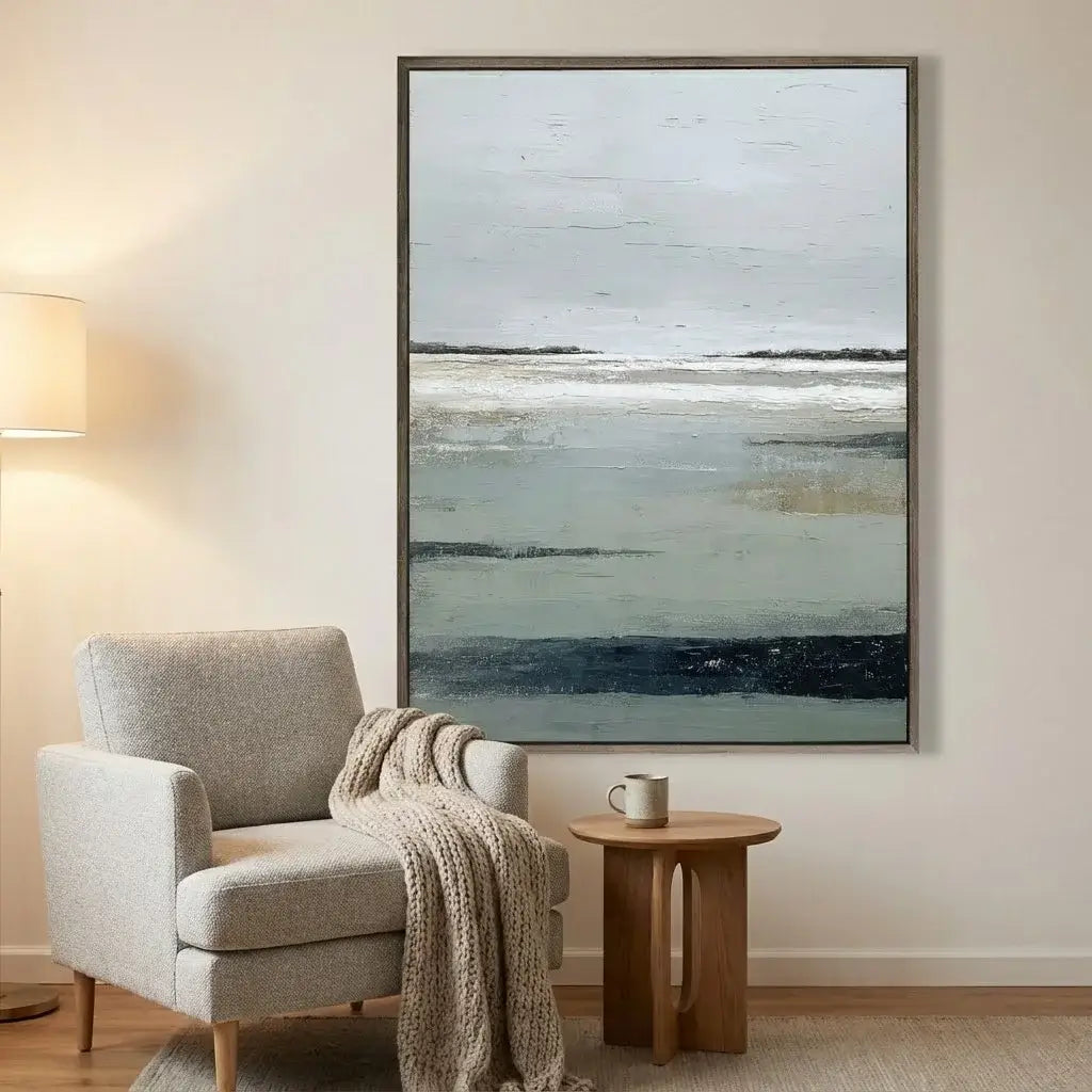 Gray armchair with a blanket and wooden side table in a room with a large abstract painting on the wall.