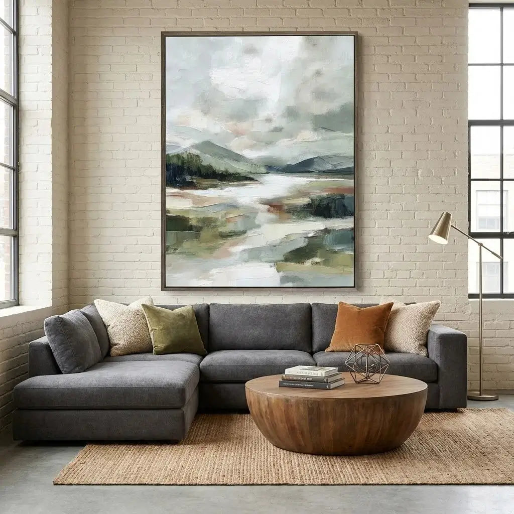 Living room with a gray sectional sofa, wooden coffee table, and abstract landscape painting on a brick wall.