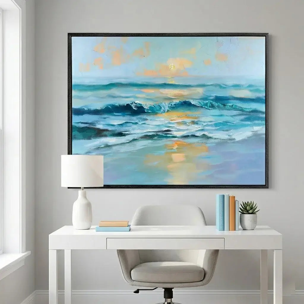 Framed beach scene painting above a desk with a lamp and chair.