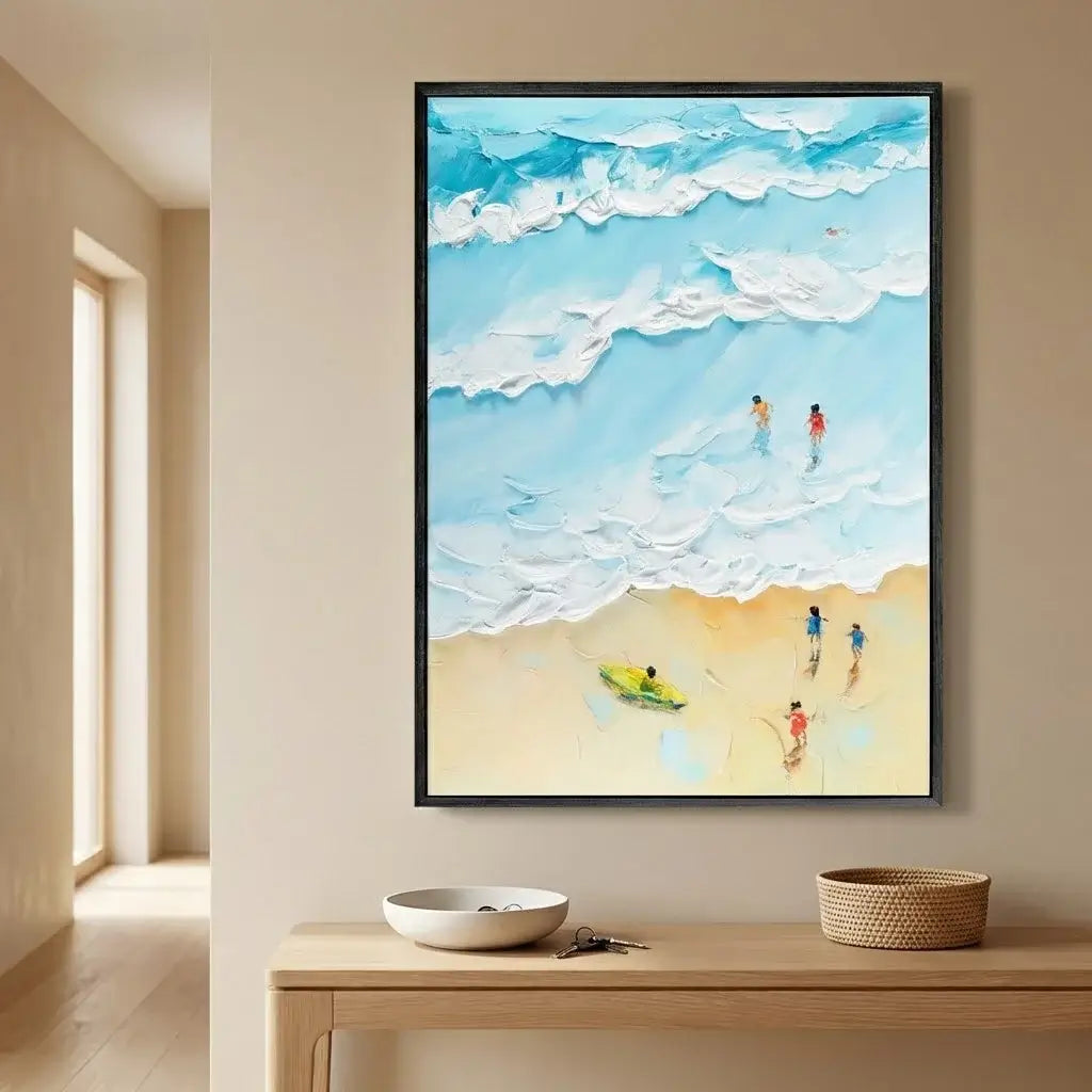 Framed artwork of a beach scene with people on a wall above a wooden table.