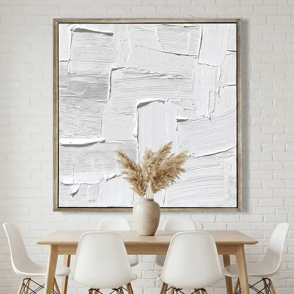 Abstract painting on a white brick wall above a wooden table with white chairs.