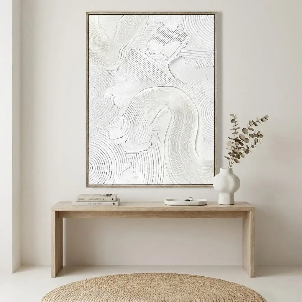 Abstract artwork in a wooden frame on a wall above a console table with decor items.
