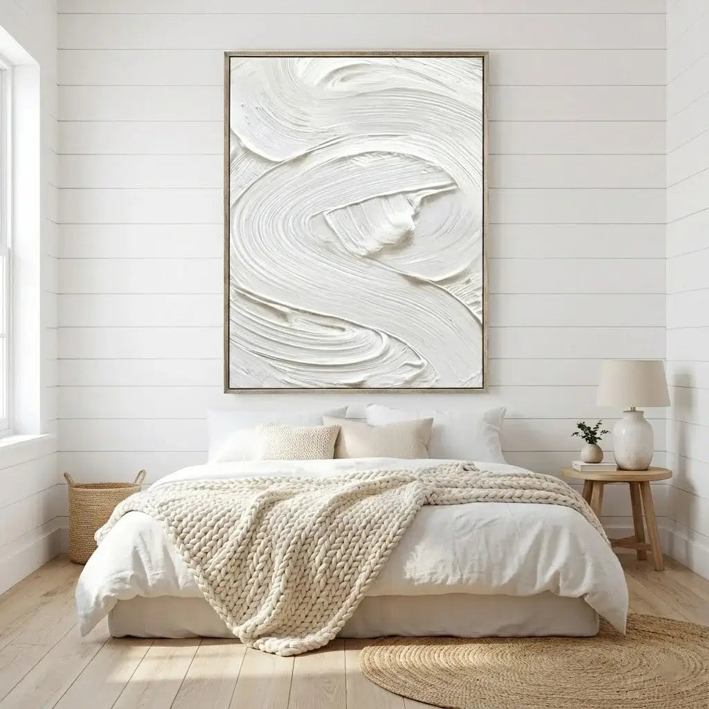 Bedroom with abstract art on the wall, bed with white bedding and beige blanket, and wooden side table.