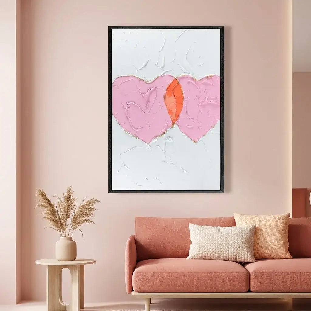 Framed abstract art with pink and orange heart on a wall above a pink sofa.