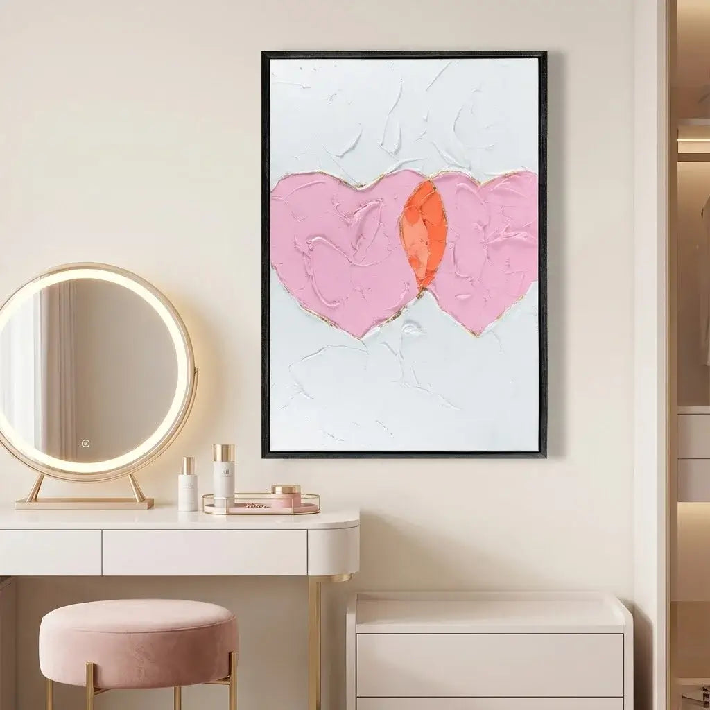 Dressing table with round mirror, pink stool, and abstract heart artwork on a white wall.