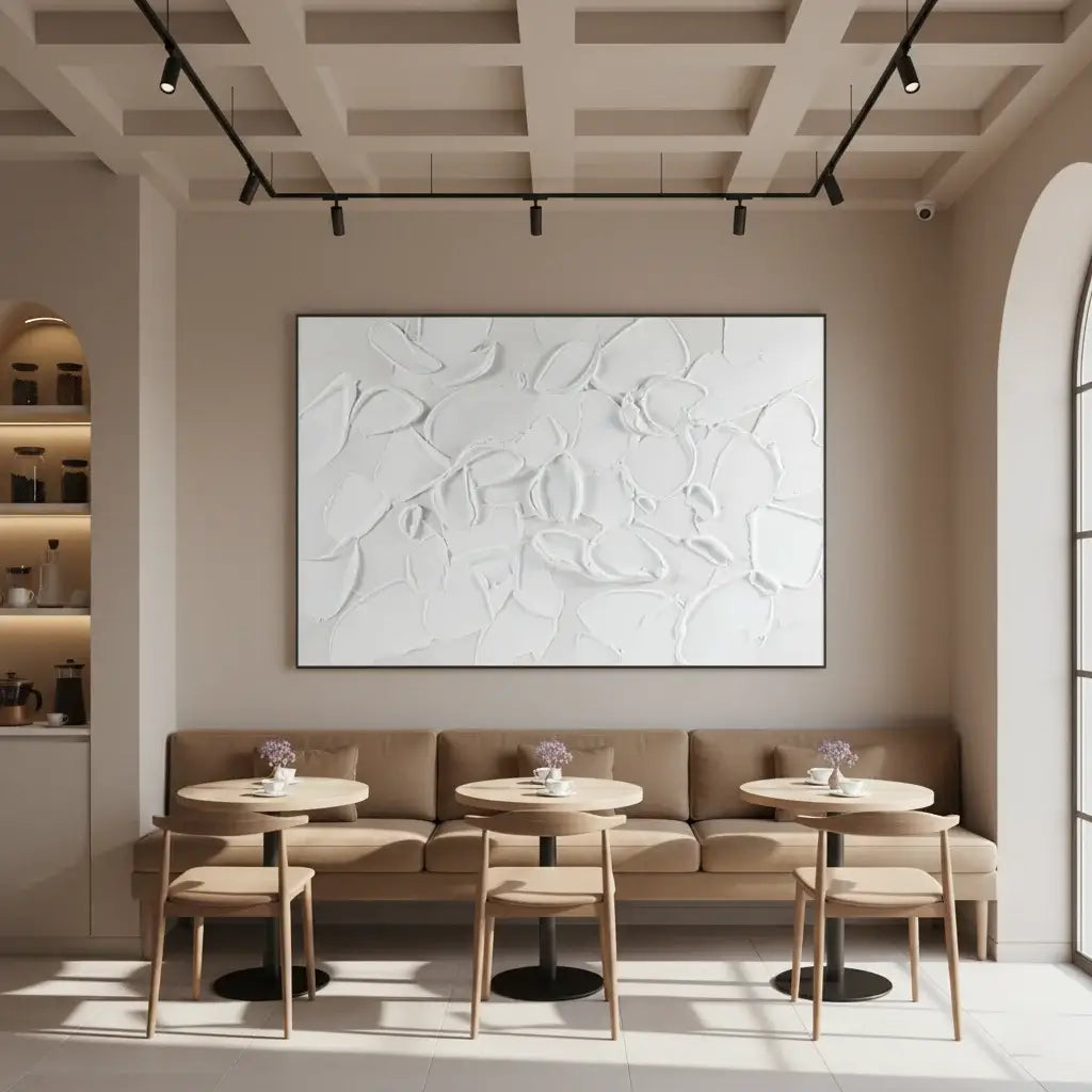 Modern cafe interior with beige walls, abstract art, and round tables with chairs.