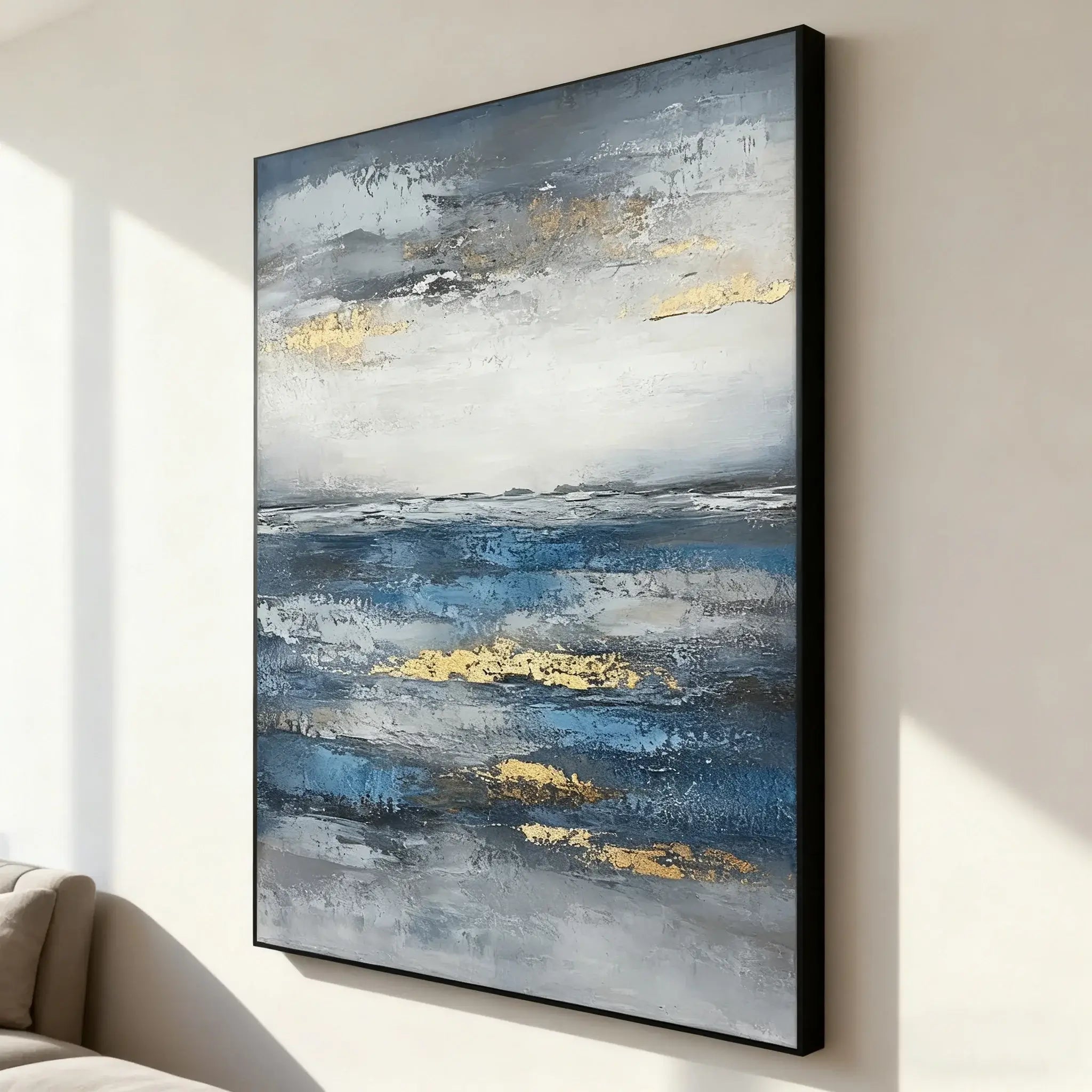 Abstract painting with gold and blue tones on a wall in a room with a couch.