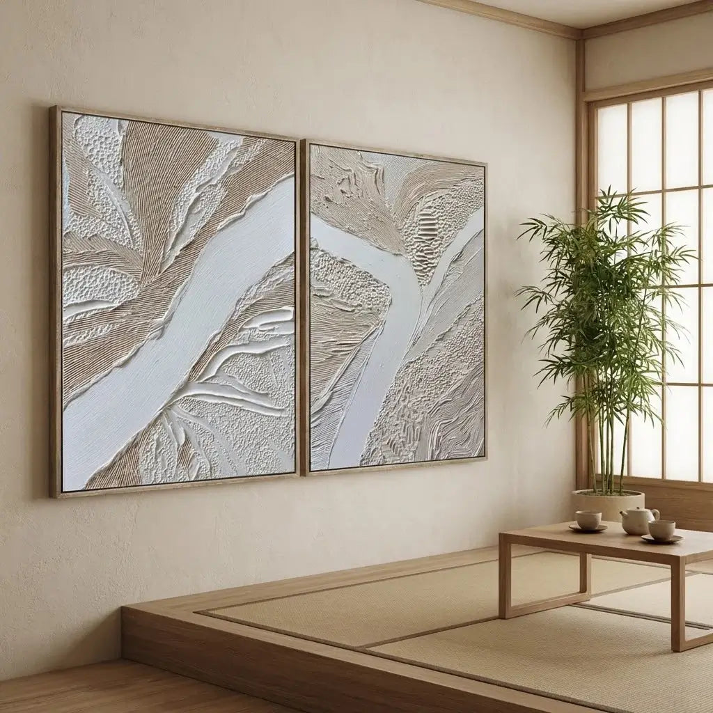 Two abstract wall art pieces on a beige wall with a wooden coffee table and plant in the foreground.