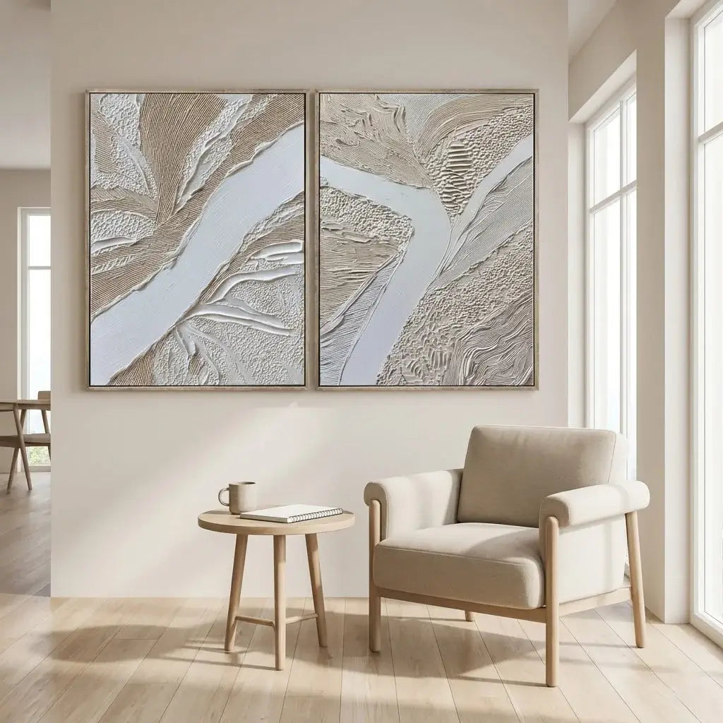 Two abstract wall art pieces above a chair and small table in a bright room.