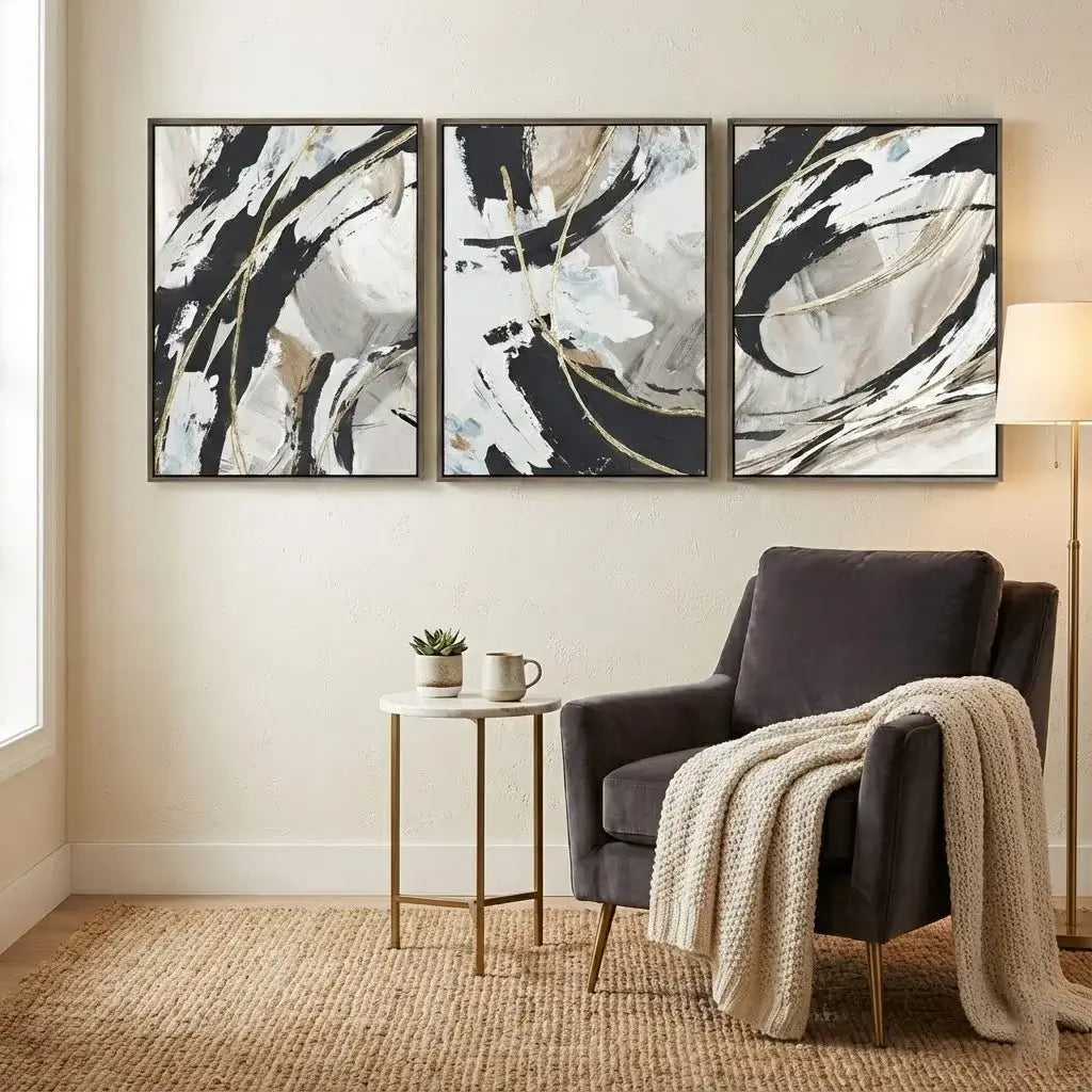 Three abstract paintings above a dark armchair with a beige blanket in a living room.