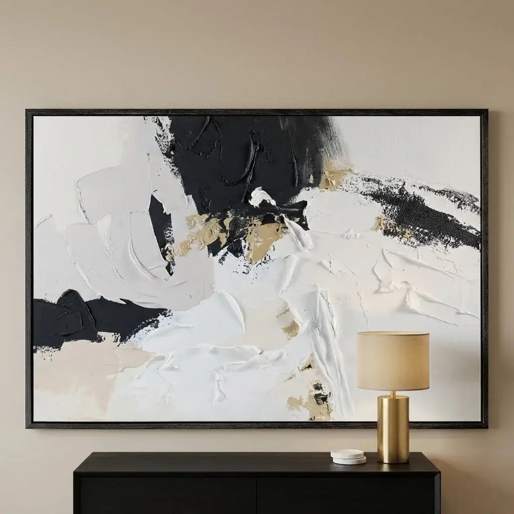 Abstract art painting with black, white, and gold on a beige wall above a dark console table with a lamp.
