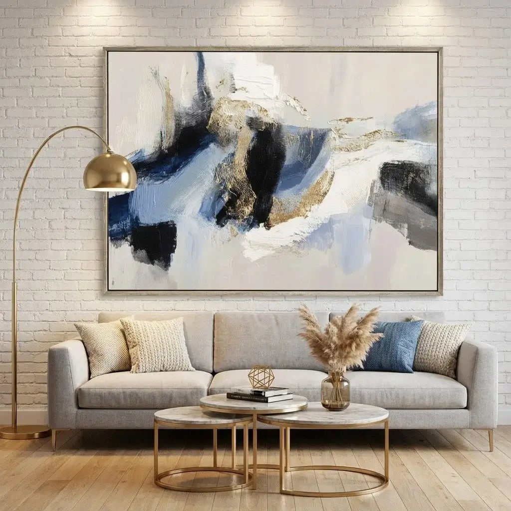 Living room with a gray sofa, gold coffee tables, and abstract art on a white brick wall.