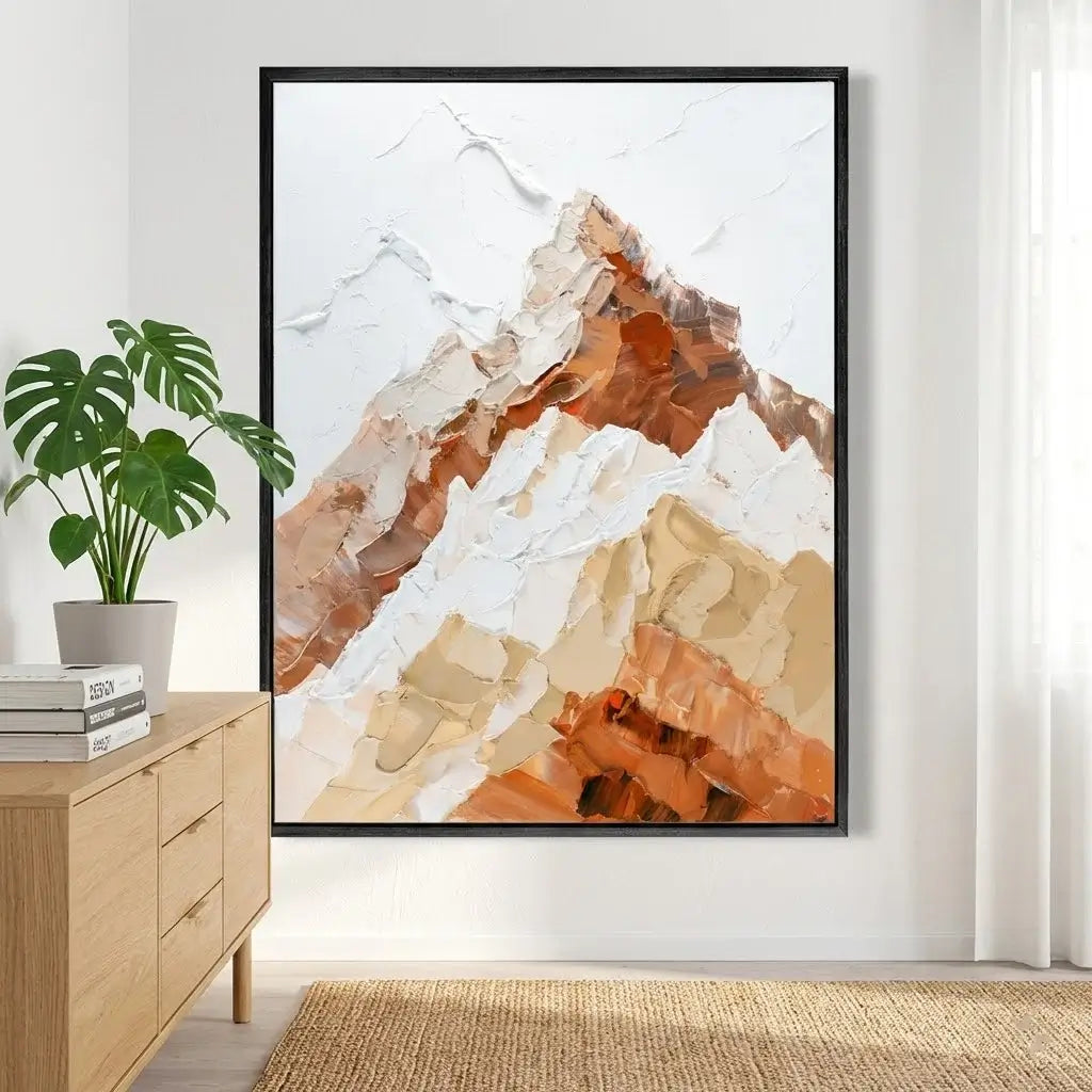Framed abstract mountain art piece on a wall with a plant and wooden cabinet below.