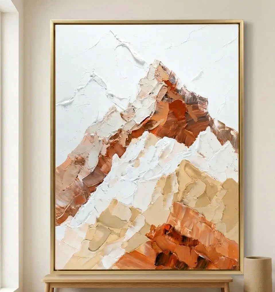 Framed abstract mountain art piece on a wall with a plant and wooden cabinet below.