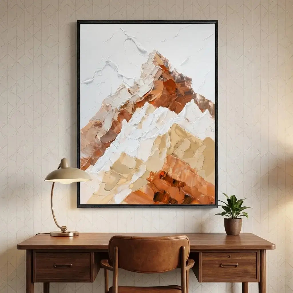 Framed abstract mountain art above a wooden desk with a lamp and plant.