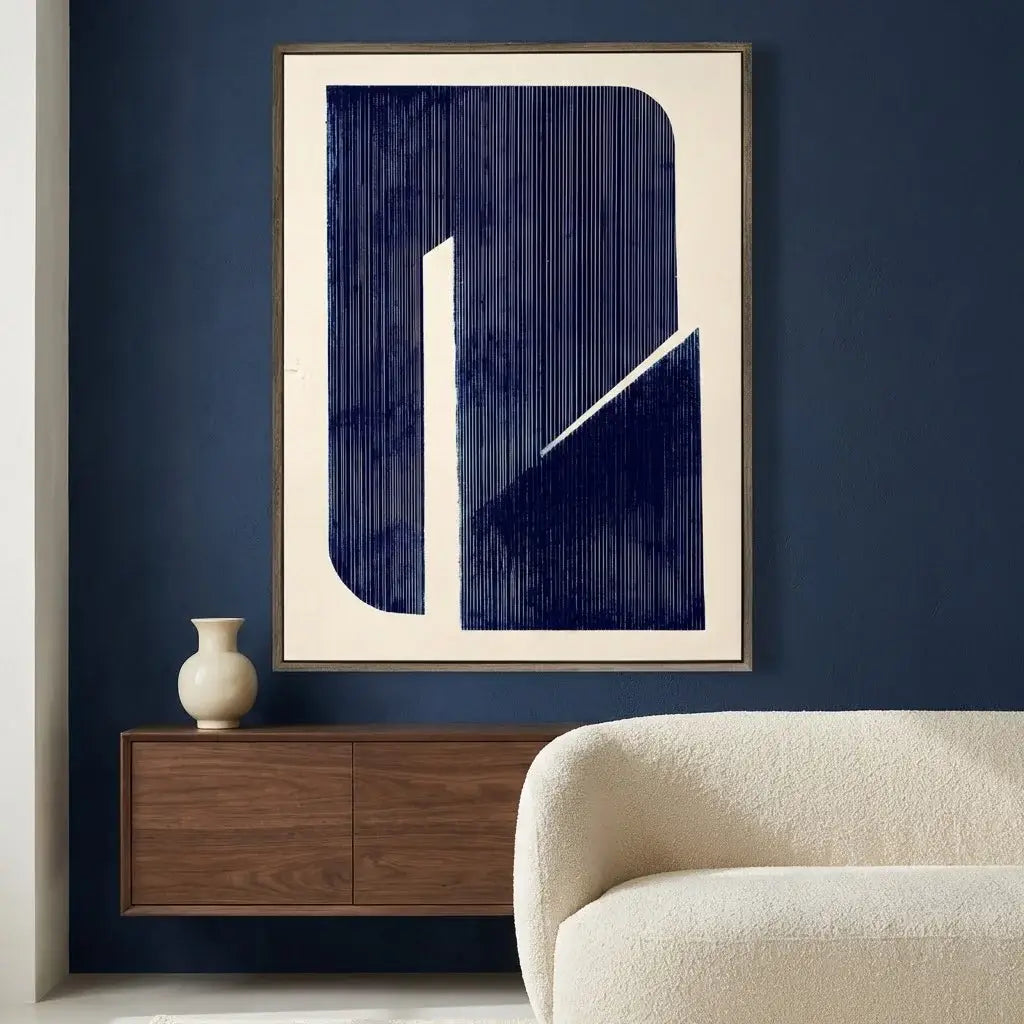 Abstract art print on a wall above a wooden cabinet with a vase and a beige sofa.