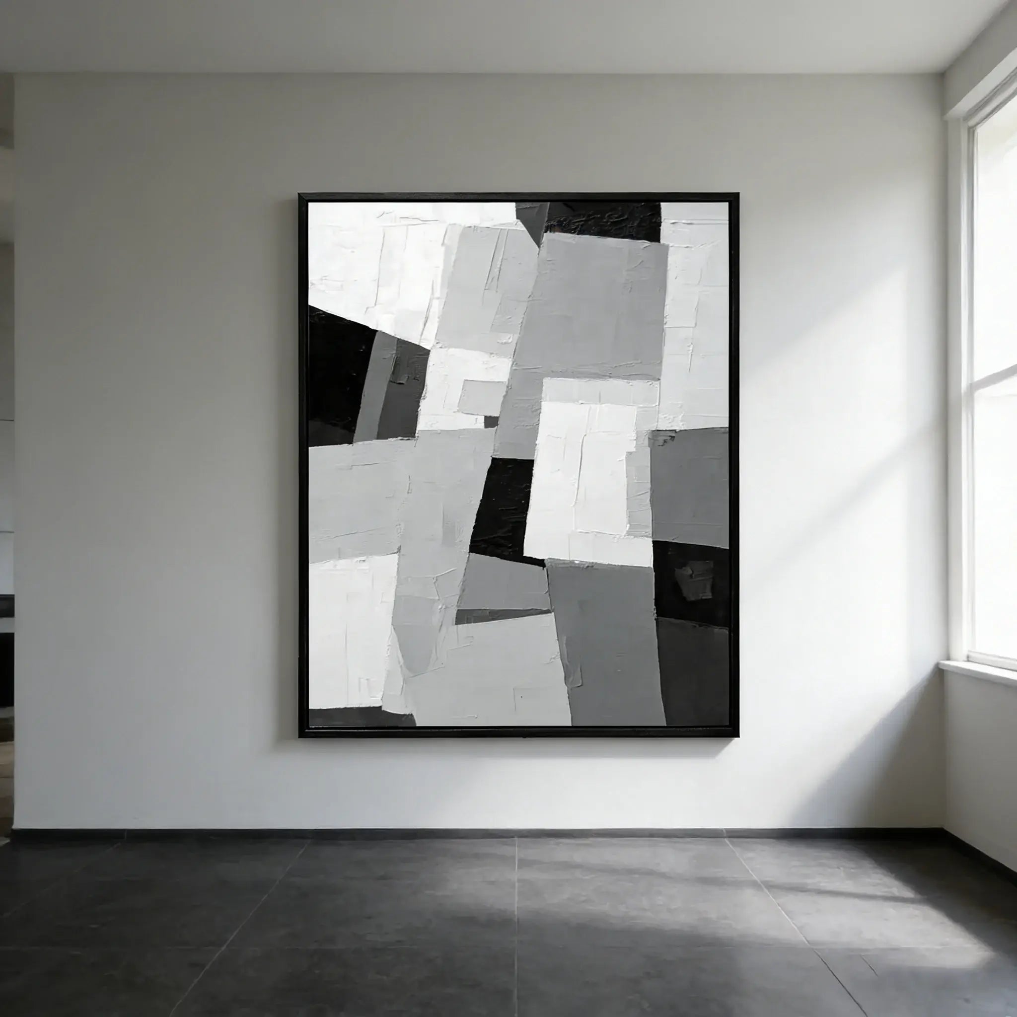 Abstract black and white artwork on a wall in a minimalistic room with natural light.