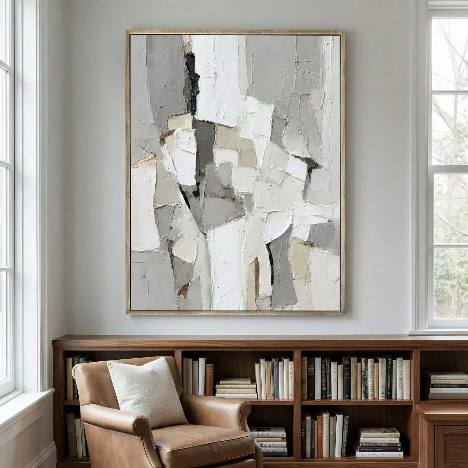 Abstract art piece on a wall above a bookshelf with a chair and books.