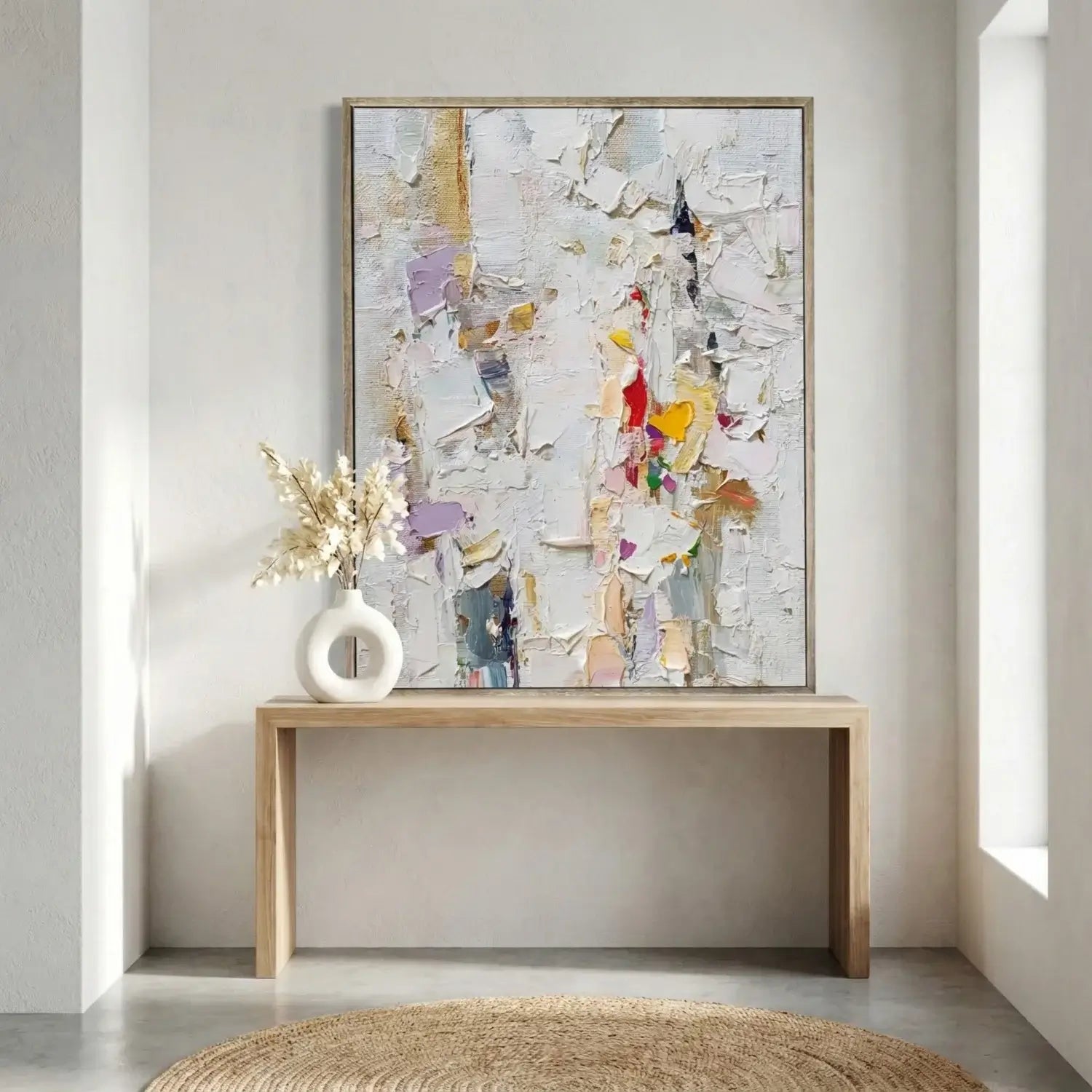 Abstract art piece on a wall above a wooden console table with a vase and flowers.