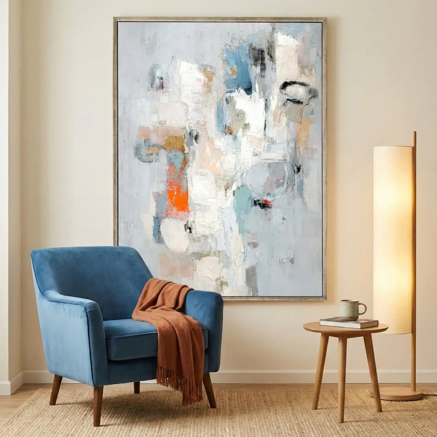 Blue armchair with a brown blanket in front of a large abstract painting on a beige wall.