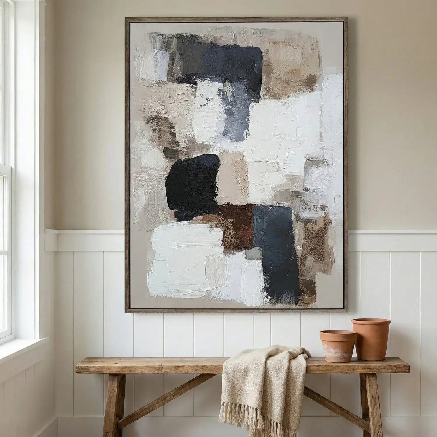 Abstract art piece on a wall above a wooden bench with pots and a blanket.