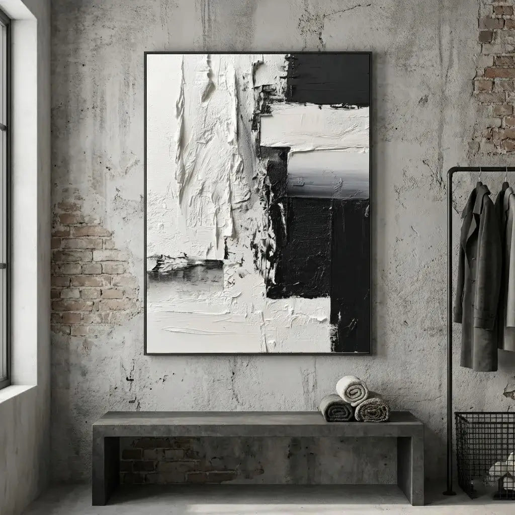 Abstract black and white painting on a textured wall with a bench and folded clothes below.