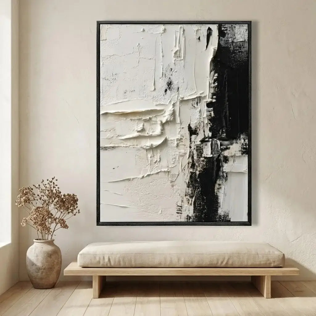 Abstract art piece in a black frame on a wall above a bench with a vase of dried flowers.