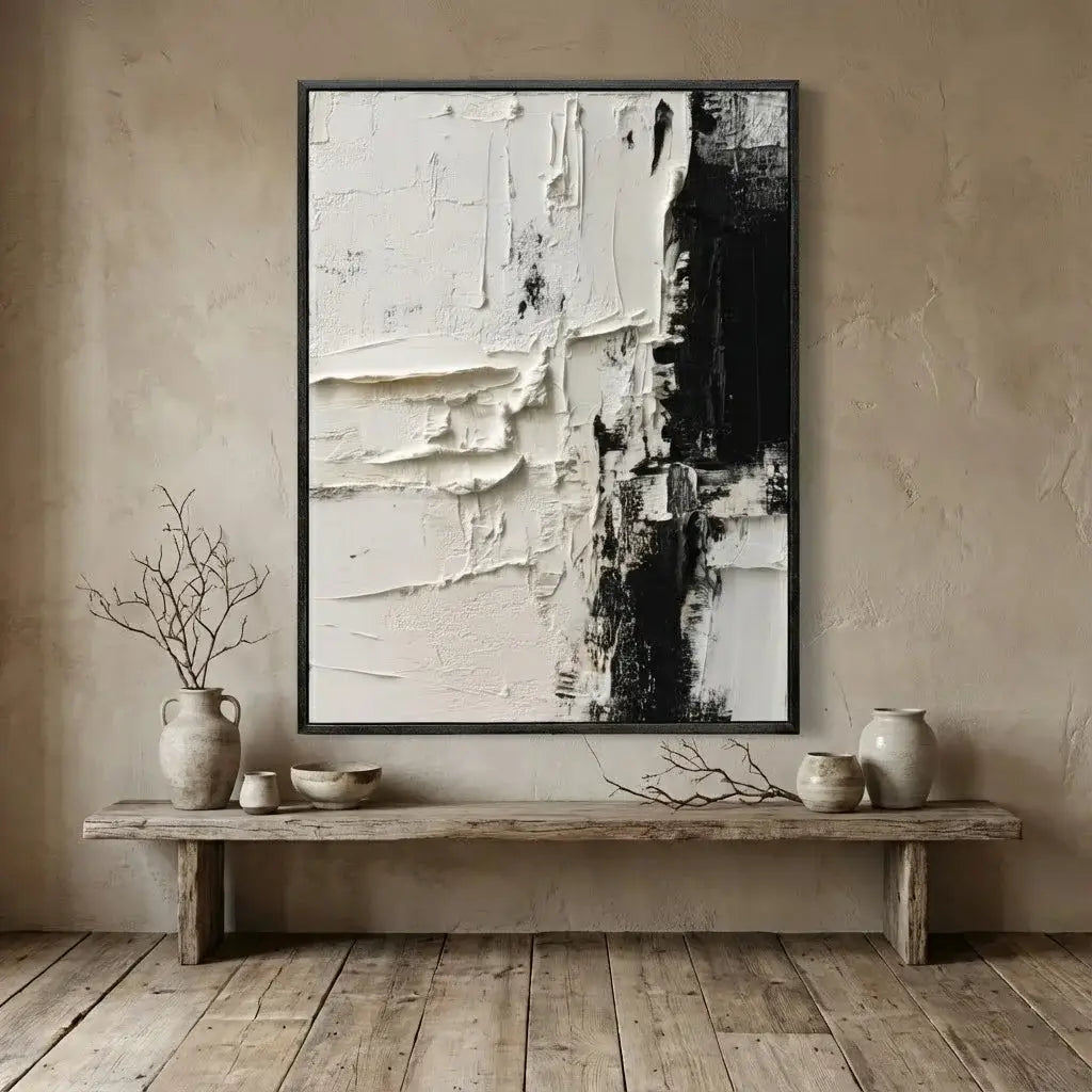 Abstract art piece in a black frame on a beige wall above a wooden bench with decorative items.
