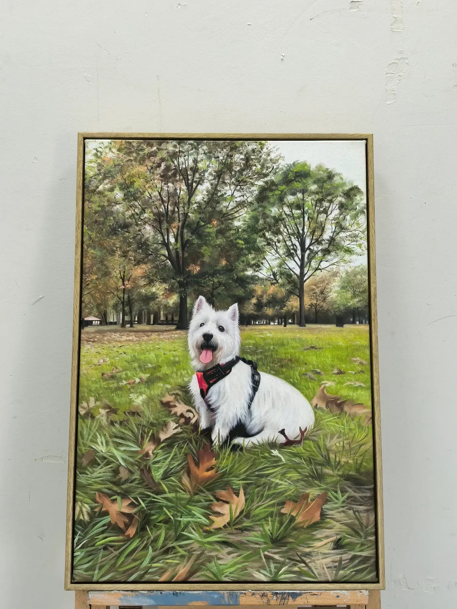 Framed painting of a white dog sitting on grass with trees in the background